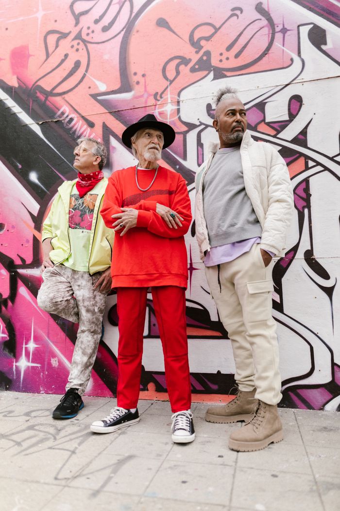 Three senior men in vibrant urban fashion against a colorful graffiti wall.